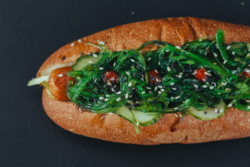 Big hotdog with sausage tomatoes, mustard and salad isolated on black background.