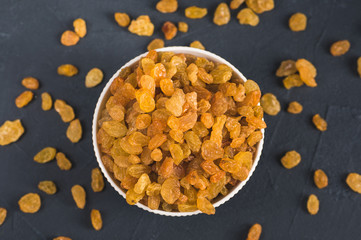 Bowl of yellow raisins on dark background