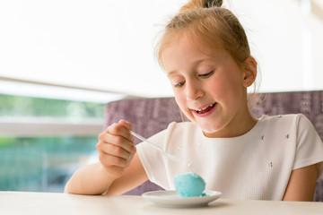 Little girl eating ice cream in a cafe. Adorable little girl eating ice cream at summer. Happy girl eating ice cream in cafe