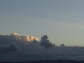 A background texture of fluffy gray clouds highlighted by afternoon sun against a dusky blue sky. 