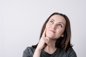 Large portrait of a young European woman on a gray background, hand touches cheek, dreamy look.