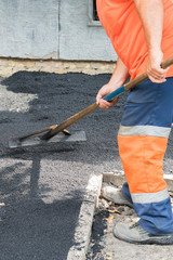 Worker man lays asphalt road repair road paving yellow sun ray light. A man in overalls is laying...