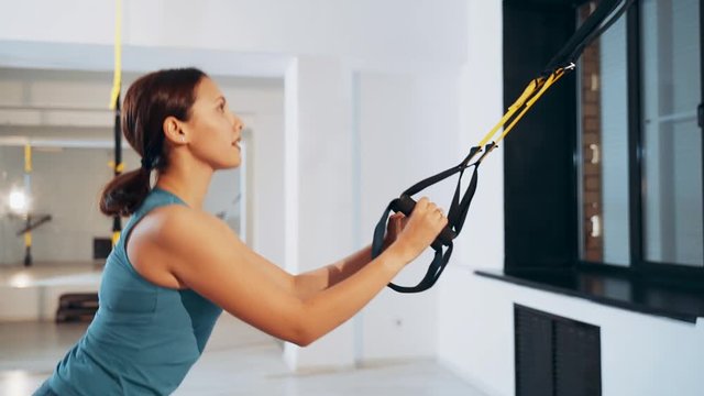 Girl performs jumping using TRX loops. Girls engaged with TRX loops.