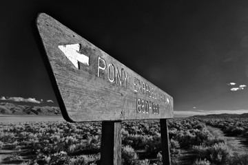 Pony Express Trail through sagebrush desert crosses highway 50 in Central Nevada . The trail is to the right of the sign heading toward the horizon 