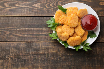 Chicken nuggets with red sauce on a plate on a brown wooden table. fast food. place for text. top view