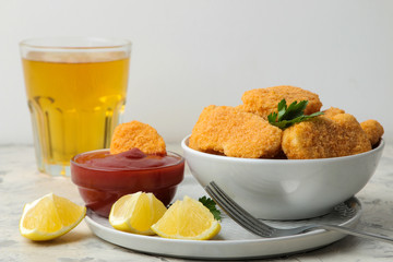 Chicken nuggets in a bowl with red sauce, ketchup and beer on a light concrete table. fast food.