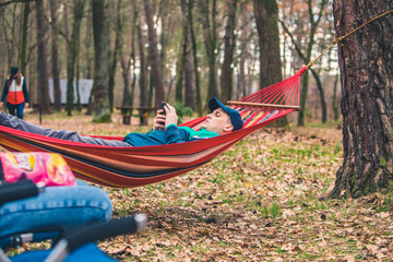 Obraz na płótnie Canvas young man laying in hammock surfing in phone