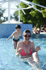 Fototapeta na wymiar 40 Years old Mom play with son in a pool. Cheerful child splashing in the swimming pool with his mother