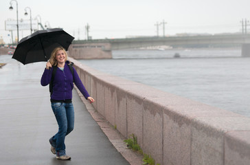 happy blonde girl with umbrella near the bridge in the city with copy space