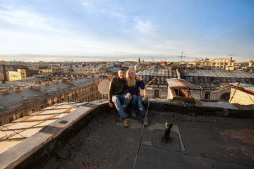 Fototapeta premium happy couple boy and girl tourists sitting on the roof with the top view of Saint Petersburg’s panorama with copy space