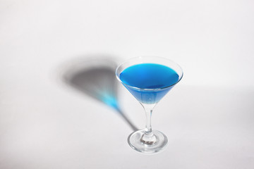 Glass goblet with blue drink on a white background. With a shadow from a glass of Minimalism.