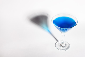 Glass goblet with blue drink on a white background. With a shadow from a glass of Minimalism.