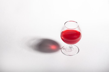 Glass goblet with red drink on a white background. With a shadow from a glass of Minimalism.