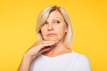 Happy smiling beautiful cute lovely blonde senior woman with beauty clean skin in casual wear isolated on yellow background. Healthcare and cosmetology concepts. Pensioner and mature people