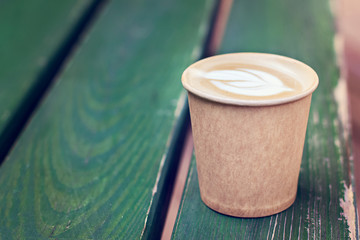 Cappuccino coffee in paper cup on the wooden old table