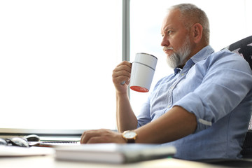 Focused mature businessman deep in thought while sitting at the desk with cup of coffee in his hand...