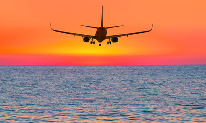 Fototapeta na wymiar Airplane flying above tropical sea at sunset