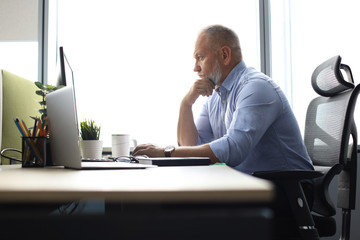 Focused mature businessman deep in thought while sitting at a table in modern office.