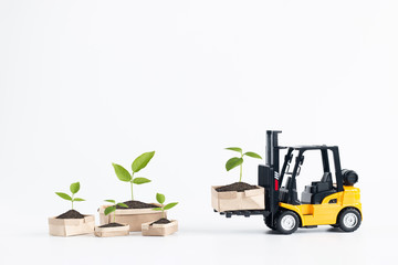 Miniature  forklift truck model loading cardboard boxes containing young plant isolated on white background with copy space for text message