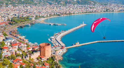 Paraglider tandem flying over marina and Red tower in Alanya peninsula, Antalya district, Turkey