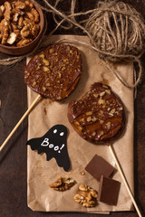 Slices of apples in chocolate, caramel glaze and walnuts on skewers on a dark background