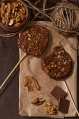 Slices of apples in chocolate, caramel glaze and walnuts on skewers on a dark background