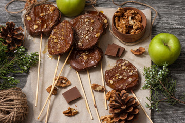 Slices of apples in chocolate, caramel glaze and walnuts on skewers on a dark background