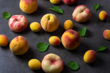 Nice yummy fresh apricots and peaches with green tree leaves on dark texture surface. Summer fruits.