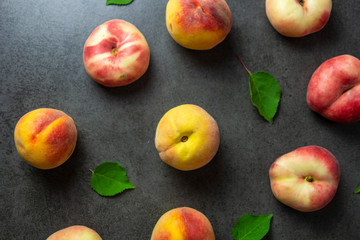 Nice yummy fresh peaches with green tree leaves on dark texture surface. Top view. Summer fruits.