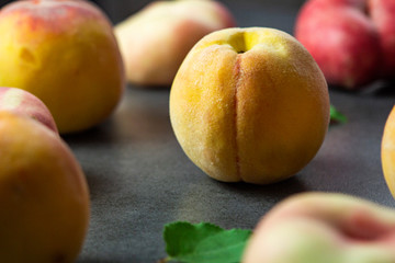 Nice yummy fresh apricots and peaches with green tree leaves on dark texture surface. Summer fruits.