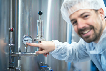 Industrial machine pressure gauge and technologist in white protective suit pointing finger to the barometer. Industrial worker reading pressure of an industrial machine in food processing factory.