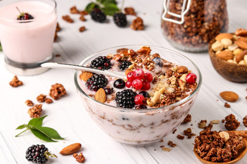 Granola crispy honey muesli with natural yogurt, fresh berries, chocolate and nuts in a bowl against a light background, healthy food, horizontal orientation