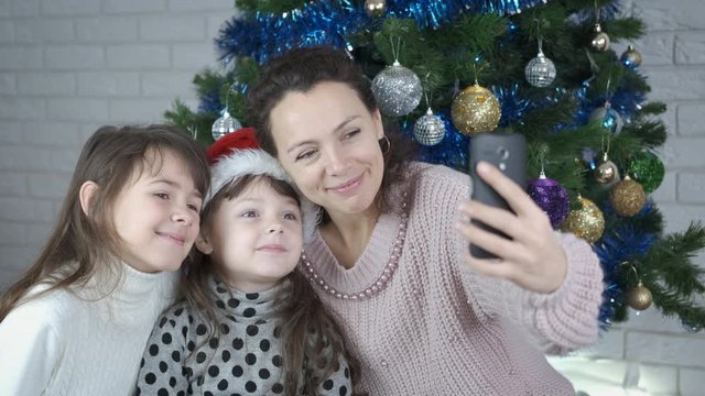 Family at Christmas takes a selfie. A mother and her daughters are photographed under the Christmas tree.