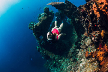 Woman freediver glides with fins at wreck ship. Freediving in blue ocean near wreck
