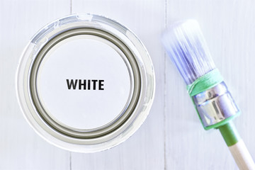 Paint can on freshly painted white wooden background and brush with green. Paint bucket with cover lid and text white in black. Home makeover decoration renovation background. Flat lay.     
