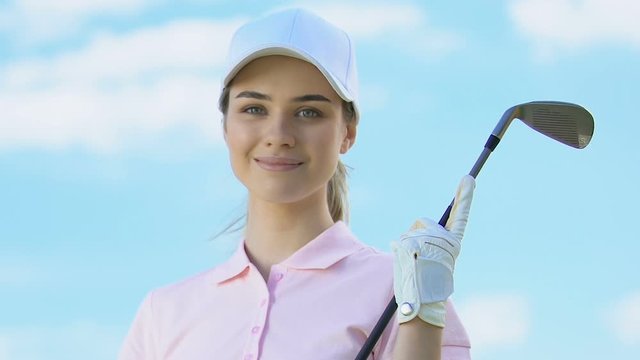 Attractive woman in golfer uniform and with club posing to camera, luxury hobby