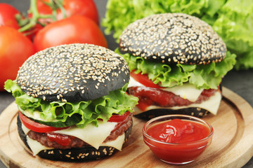 Two black burgers with vegetables and beef meat