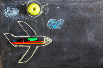 Back to school. Chalked drawing of an airplane on a school blackboard with school supplies and an empty place for your text or design.