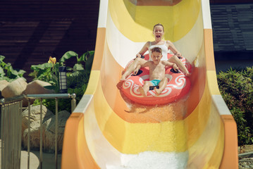 People having fun at aquapark. Son and mother gliding down slide together.