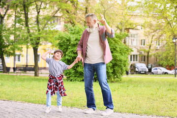 Cute little boy and his grandfather walking in park