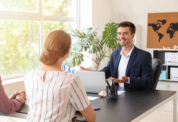 Male travel agent working with young couple in office