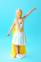 Cute little girl dressed as superhero on color background