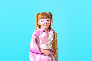 Cute little girl dressed as superhero on color background