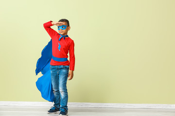 Cute African-American boy dressed as superhero near color wall