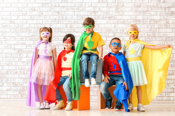 Obraz premium Cute little children dressed as superheroes near brick wall