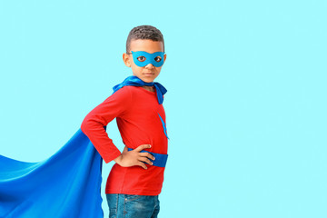 Cute African-American boy dressed as superhero on color background