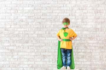 Cute little boy dressed as superhero near brick wall