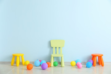 Chair, stools and balloons near color wall in children's room