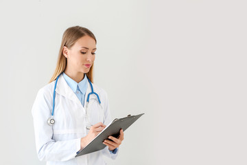 Female doctor with stethoscope and clipboard on light background