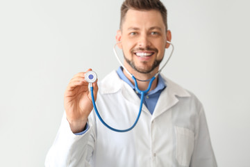 Male doctor with stethoscope on light background